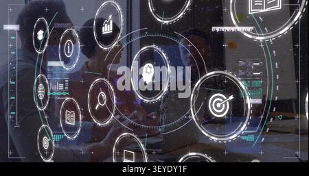 Center person typing on laptop, team comparing notes, HUD icons rotating over glass for designers Stock Photo