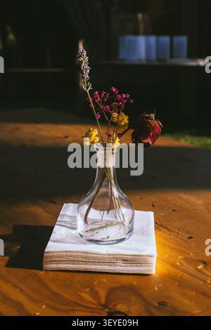 Arrangement of dried flowers in a clear glass vase on a folded white napkin on a wooden table with natural light Stock Photo