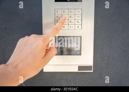 Person entering numbers on residential building intercom keypad. Secure access control enables visitor communication and controlled building entry Stock Photo