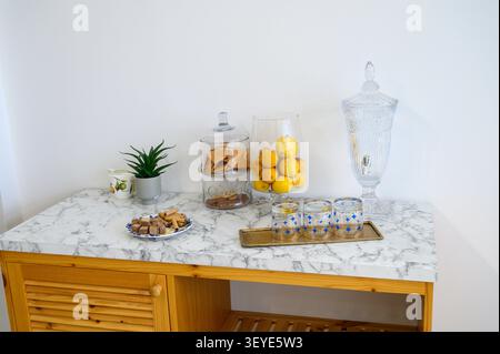 Brightly lit tabletop showcases fresh lemons, snacks, and decorative glassware in a cozy setting. Stock Photo