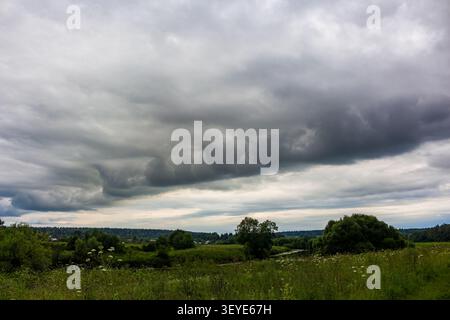 Dramatic shelf cloud looming over a lush green summer meadow, ominous rolling storm front forming in the heavy grey sky before a powerful weather even Stock Photo