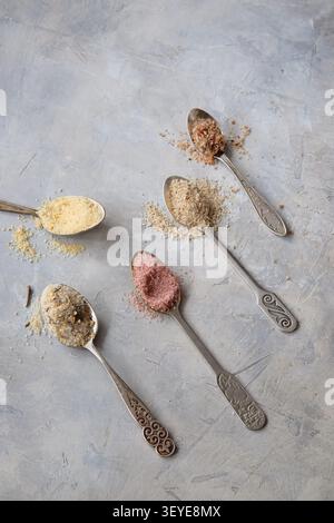 Vintage spoons holding colorful coarse salt on textured gray plaster surface display Stock Photo
