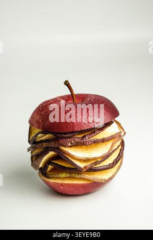 Deconstructed red apple with layered dried slices and water droplets on clean white background Stock Photo