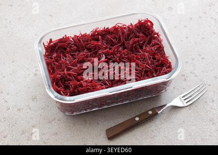 Fresh grated beetroot salad in a glass food container with fork on a light stone surface. Healthy vegetable dish, meal prep ingredient Stock Photo