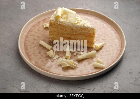 Layered cake slice with white chocolate curls on ceramic plate over gray background Stock Photo