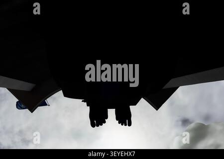 Minimalist low-angle photograph capturing the silhouetted feet of a monumental statue against a dramatic cloudy sky. The striking perspective emphasiz Stock Photo