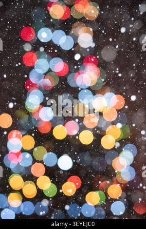 Vertical festive background featuring warm glowing Christmas tree bokeh lights against a soft brown background. Gentle falling snow creates a cozy hol Stock Photo