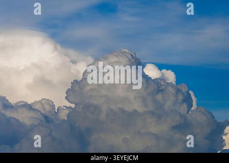 Stunning and dense formation of fluffy clouds with white and grey textures under a bright blue sky during daytime. Stock Photo