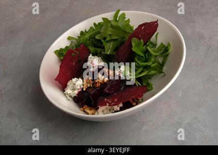 Fresh beet salad with arugula, goat cheese and walnuts in white bowl on stone surface Stock Photo