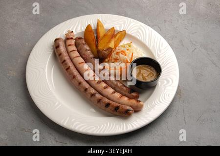 Grilled sausages with potato wedges, sauerkraut and dipping sauce on ceramic plate Stock Photo