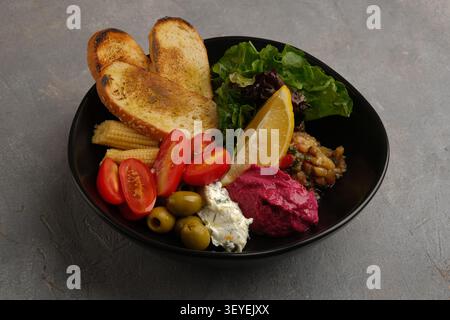 Colorful Mediterranean salad bowl with toasted bread, vegetables, olives, lemon, and dips Stock Photo