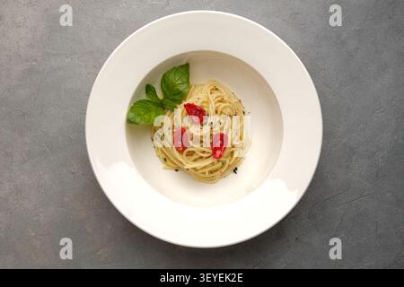 Spaghetti with basil and roasted tomatoes served on white plate over gray stone surface Stock Photo