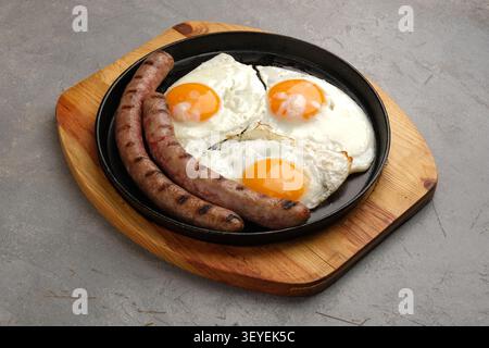 Grilled sausages with fried eggs in cast iron skillet on rustic wooden board Stock Photo