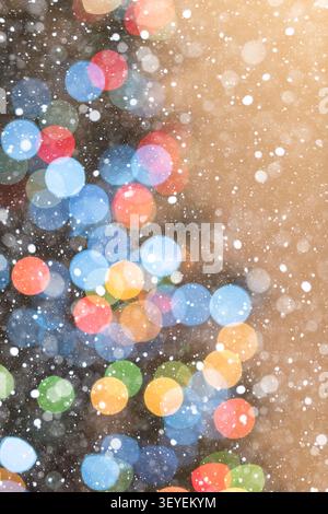 Vertical festive background featuring part of a decorated Christmas tree with warm glowing bokeh lights against a soft brown background. Falling snow Stock Photo