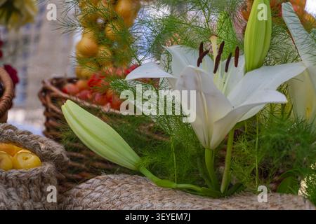 Elegant white lily surrounded by fresh cherries, greenery and rustic decorations creating a beautiful summer floral arrangement with natural seasonal Stock Photo