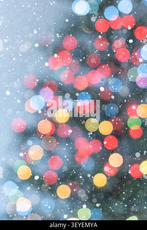 Vertical holiday background featuring multicolored Christmas tree bokeh lights on a soft light blue background. Falling snow and the subtle outline of Stock Photo