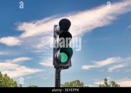 Green traffic light shining against a blue sky with clouds Stock Photo