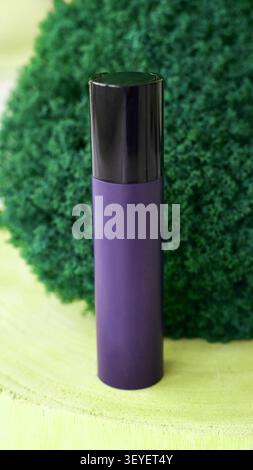 Purple Cylindrical Bottle Standing Upright On Green Moss Covered Wooden Surface Close Up Product Display With Black Cap Vertical Composition Natural Backdrop For Cosmetic Branding. Stock Photo