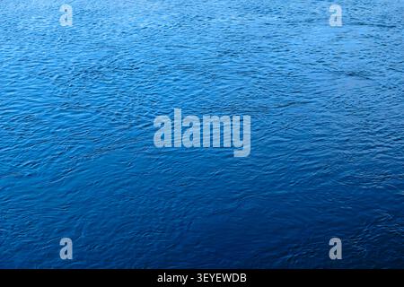 Deep blue water fills the frame. Gentle ripples create soft waves. Smooth surface reflects light. Close-up perspective shows water texture. Calm body Stock Photo