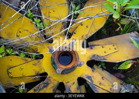 An old mechanical metal cooling fan lying on the ground, with a puddle of water at its center; photo taken in a junkyard full of truck and excavator p Stock Photo