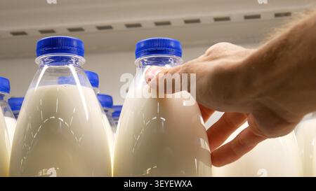 Close-up of many plastic milk bottles with blue caps and a male buyer's hand takes one Stock Photo