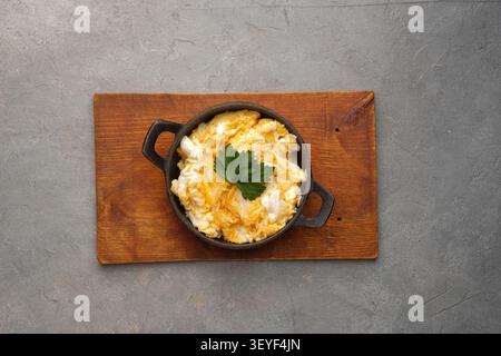 Rustic skillet of creamy scrambled eggs with parsley on wooden board over gray stone surface Stock Photo
