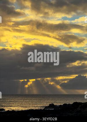 Sunset over the ocean beneath dramatic clouds, with golden light ...