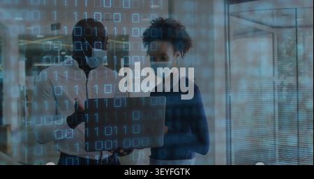 Man leaning in starting data review, masked team holding laptop, pointing, nodding, binary overlay Stock Photo