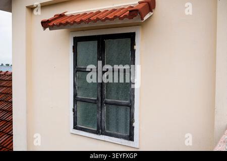 Close-up view of a wooden shuttered window with a curved tiled awning in Hoi An Stock Photo