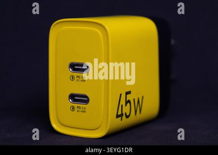 A charger with a bright yellow design has two USB-C ports for quick charging of various electronic devices. It is shown against a dark background. Stock Photo