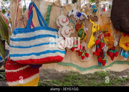 Handmade market stall showcasing a vibrant collection of artisanal products, featuring striped crochet bags, small knitted hats, fruit keychains, and Stock Photo