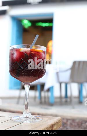 Refreshing cocktail in a decorative glass with fruit garnishes placed on a wooden table, vibrant restaurant interior visible in the background Stock Photo