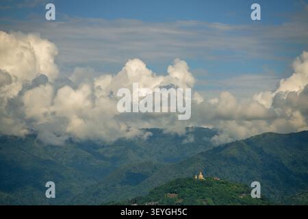 Scenic green mountains covered with dense forest and orthodox church standing on hilltop under dramatic cumulus clouds. Georgia, Batumi. Stock Photo