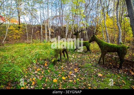 Moss-covered deer sculptures in a forested area surrounded by autumn foliage and colorful leaves on the ground Stock Photo