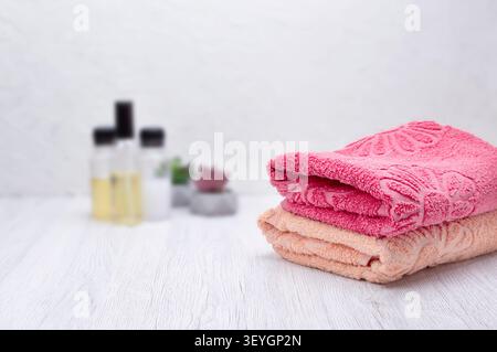 Stack of clean pink towels in a bathroom with shampoo, conditioner, and soap, side view and space for branding or text. Stock Photo