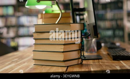 Multiple computer monitors show virtual assistant and blue display on interfaces at library study desk. Space with stacked books, green lamps and keyboards in computer lab. Stock Photo