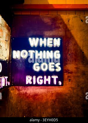 Illuminated neon sign on a textured wall & concrete background displaying the text WHEN NOTHING GOES RIGHT, malaysia Stock Photo
