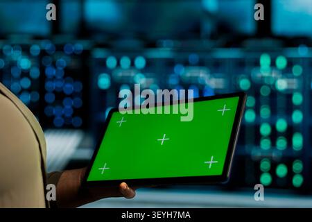 System operator uses a green screen tablet in a data center for backend troubleshooting, screen replacement, and server workflow monitoring. Stock Photo