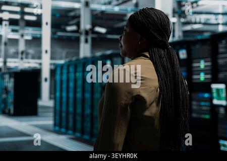 IT professional walking in server facility with mainframes supporting business needs. Data center staff member doing checkup, supporting electronics work at optimum performance for smooth operations. Stock Photo