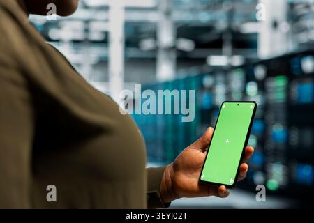 Data center programmer works with a chroma key smartphone, using an editable screen to review performance data. Stock Photo