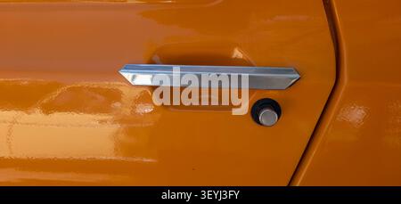TAVERNES BLANQUES, SPAIN - JUNE 14, 2026.Close-up view shows a shiny chrome door handle set against the bright orange surface of a classic Renault TL. Stock Photo