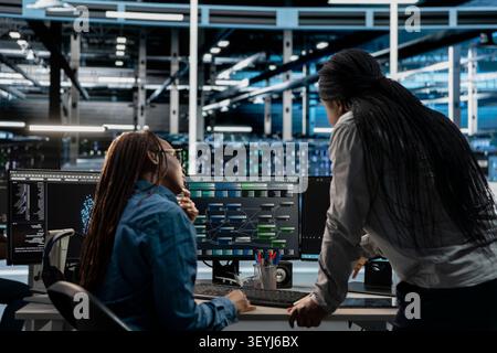 Technicians work together in a server farm, running code on a PC to repair data center racks and manage computational operations. Stock Photo