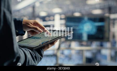Server room employee reviews tablet data charts to track system health. Stock Photo