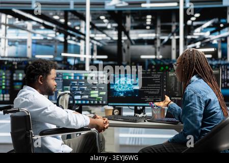 Worker using a wheelchair in a data center uses a computer to manage machine learning workloads, working with AI technology and high performance systems. Stock Photo