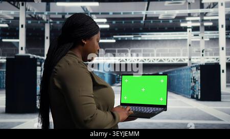 IT specialist uses a chroma key laptop in a data center for diagnostics, server monitoring and screen replacement. Stock Photo