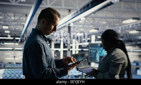 Data center technician monitors operational metrics on tablet inside a server room to improve infrastructure performance. Stock Photo