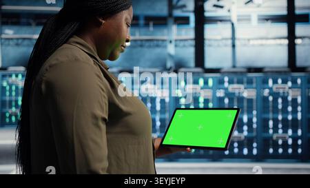 Data center administrator works with a chroma key tablet, using an editable screen to manage technical tasks. Stock Photo