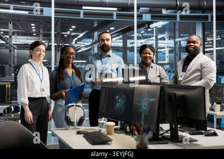 Cheerful engineering team working in server environment, analyzing data. Happy teamworking employees examining infrastructure in server facility, supporting system integrity and security. Stock Photo