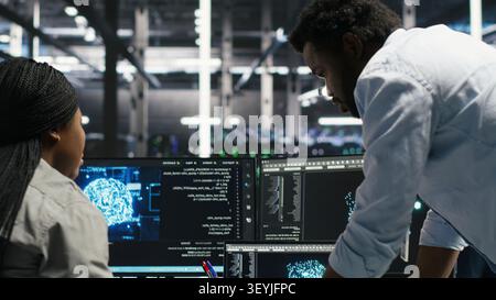 Server facility engineering team works with AI ML models to set up equipment. Teamworking colleagues work on AI programming tools in server environment, optimizing system. Stock Photo
