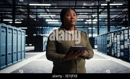 Data center administrator uses a tablet to roll out new server architecture, supporting reliable infrastructure operations. Stock Photo